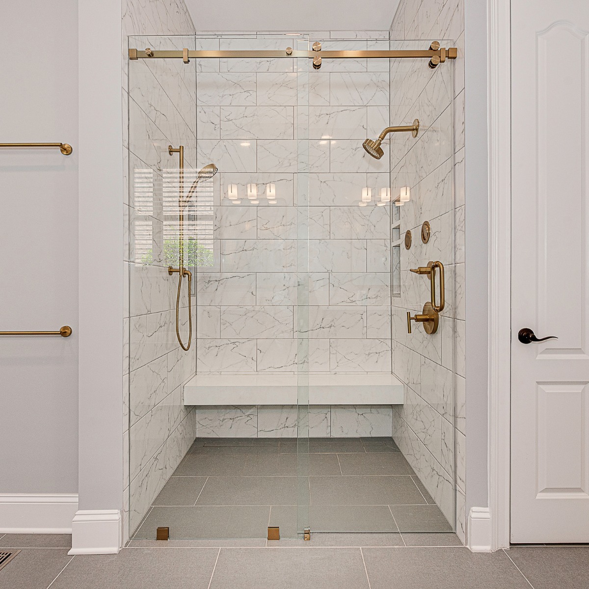Walk-in shower remodel with marble tile walls, glass enclosure, and brass fixtures