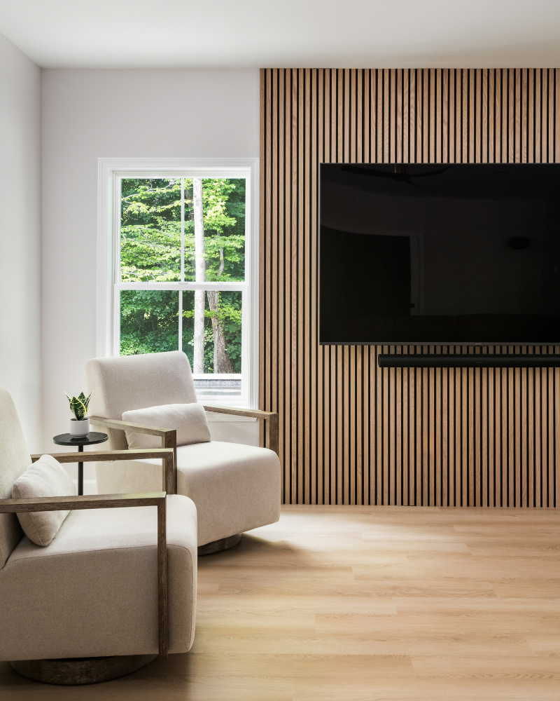 Full-height natural wood slat media wall beside a new window, with two cream swivel chairs in a finished basement Full-height natural wood slat media wall beside a new window, with two cream swivel chairs in a finished basement