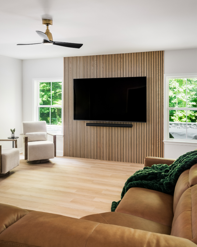 Basement great room with a full-height wood slat media wall centered between two windows and a cognac leather sectional Basement great room with a full-height wood slat media wall centered between two windows and a cognac leather sectional