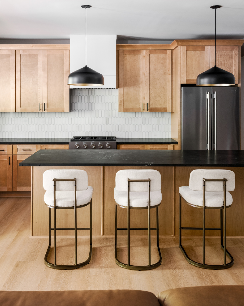 Black quartzite island with three cream upholstered counter stools on brass frames and black dome pendants above Black quartzite island with three cream upholstered counter stools on brass frames and black dome pendants above