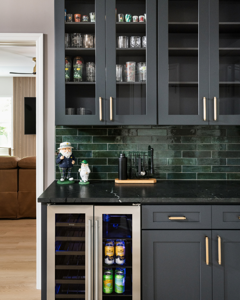 Golf room dry bar with charcoal shaker cabinets, glass-front uppers, deep green tile backsplash, brass pulls, and a dual-zone beverage refrigerator Golf room dry bar with charcoal shaker cabinets, glass-front uppers, deep green tile backsplash, brass pulls, and a dual-zone beverage refrigerator